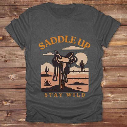 Saddle Up Stay Wild western t-shirt features a bold desert sunset graphic with a classic saddle and western landscape. Perfect for cowgirls, cowboys, and horse lovers, this rustic tee blends adventure with comfort and country charm. Whether you're heading to a rodeo, trail ride, or simply embracing your wild side, this shirt offers a soft fit and bold design. Designed for western wear fans, equestrians, and country souls, it's a must have for anyone who lives the saddle life. 