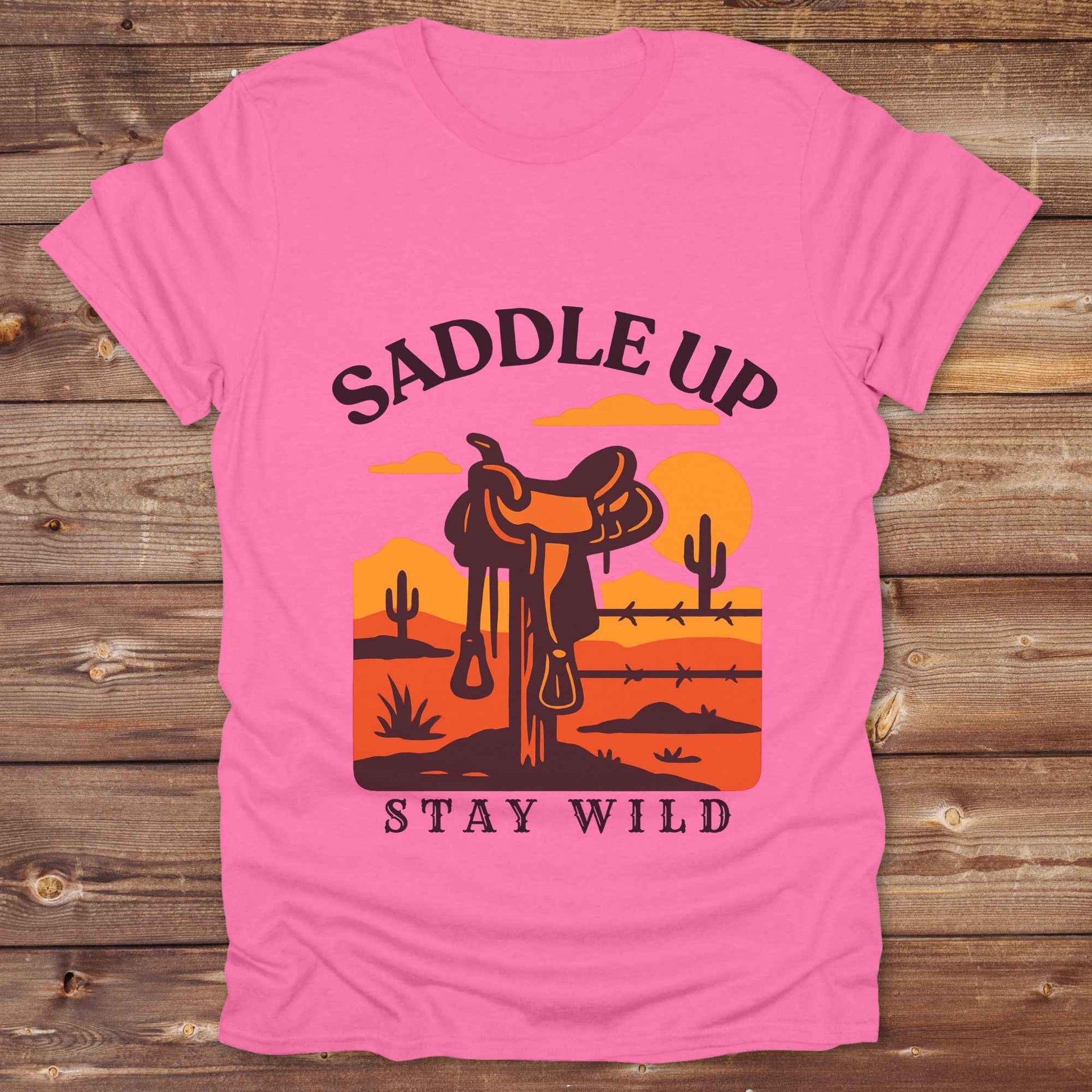 Saddle Up Stay Wild western t-shirt features a bold desert sunset graphic with a classic saddle and western landscape. Perfect for cowgirls, cowboys, and horse lovers, this rustic tee blends adventure with comfort and country charm. Whether you're heading to a rodeo, trail ride, or simply embracing your wild side, this shirt offers a soft fit and bold design. Designed for western wear fans, equestrians, and country souls, it's a must have for anyone who lives the saddle life. 