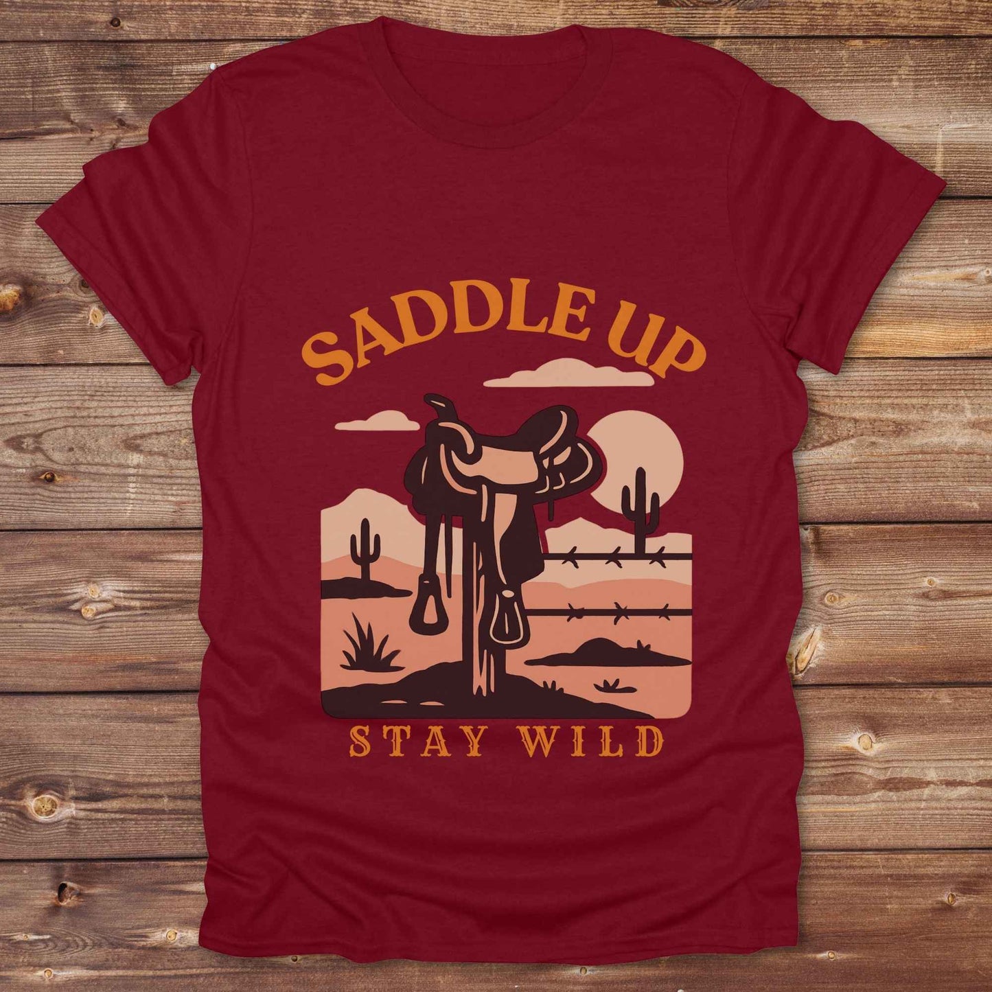 Saddle Up Stay Wild western t-shirt features a bold desert sunset graphic with a classic saddle and western landscape. Perfect for cowgirls, cowboys, and horse lovers, this rustic tee blends adventure with comfort and country charm. Whether you're heading to a rodeo, trail ride, or simply embracing your wild side, this shirt offers a soft fit and bold design. Designed for western wear fans, equestrians, and country souls, it's a must have for anyone who lives the saddle life. 