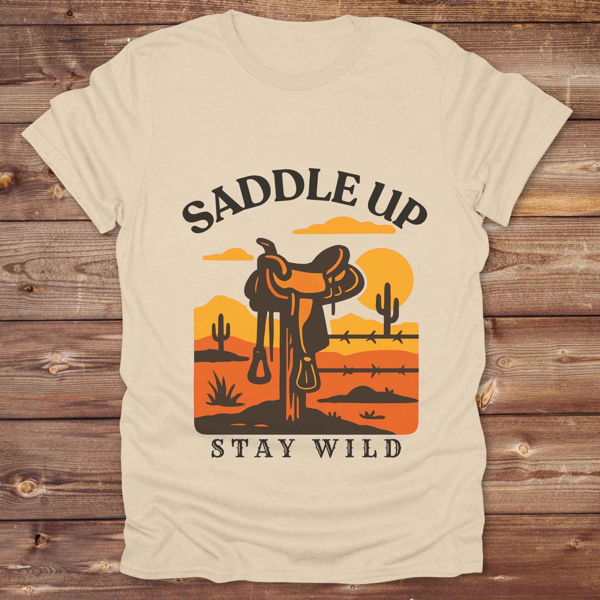 Saddle Up Stay Wild western t-shirt features a bold desert sunset graphic with a classic saddle and western landscape. Perfect for cowgirls, cowboys, and horse lovers, this rustic tee blends adventure with comfort and country charm. Whether you're heading to a rodeo, trail ride, or simply embracing your wild side, this shirt offers a soft fit and bold design. Designed for western wear fans, equestrians, and country souls, it's a must have for anyone who lives the saddle life. 