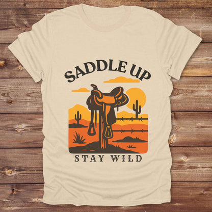 Saddle Up Stay Wild western t-shirt features a bold desert sunset graphic with a classic saddle and western landscape. Perfect for cowgirls, cowboys, and horse lovers, this rustic tee blends adventure with comfort and country charm. Whether you're heading to a rodeo, trail ride, or simply embracing your wild side, this shirt offers a soft fit and bold design. Designed for western wear fans, equestrians, and country souls, it's a must have for anyone who lives the saddle life. 