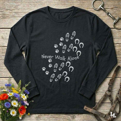 Black long-sleeve shirt with 'Never Walk Alone' design on a wooden surface with flowers and horse equipment.