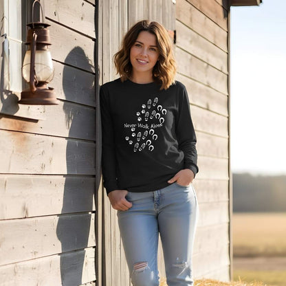 Woman wearing a black sweatshirt with text and graphics, standing against a wooden building. Never Walk Alone Long Sleeve Tee for Horse Lovers, Equestrian Apparel, Trail Riding Tee
