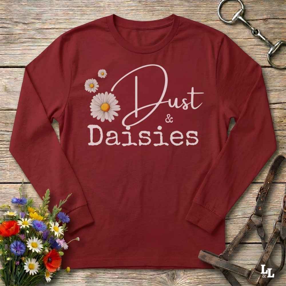 A long-sleeve crewneck shirt in deep burgundy red, laid flat on a rustic wooden surface. The shirt features a white graphic print that reads 'Dust & Daisies' accompanied by three white daisies with yellow centers.
